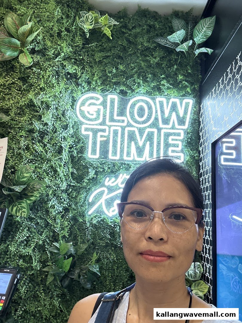 A woman stands in front of a vibrant green wall with a glowing 'GLOW TIME' neon sign.