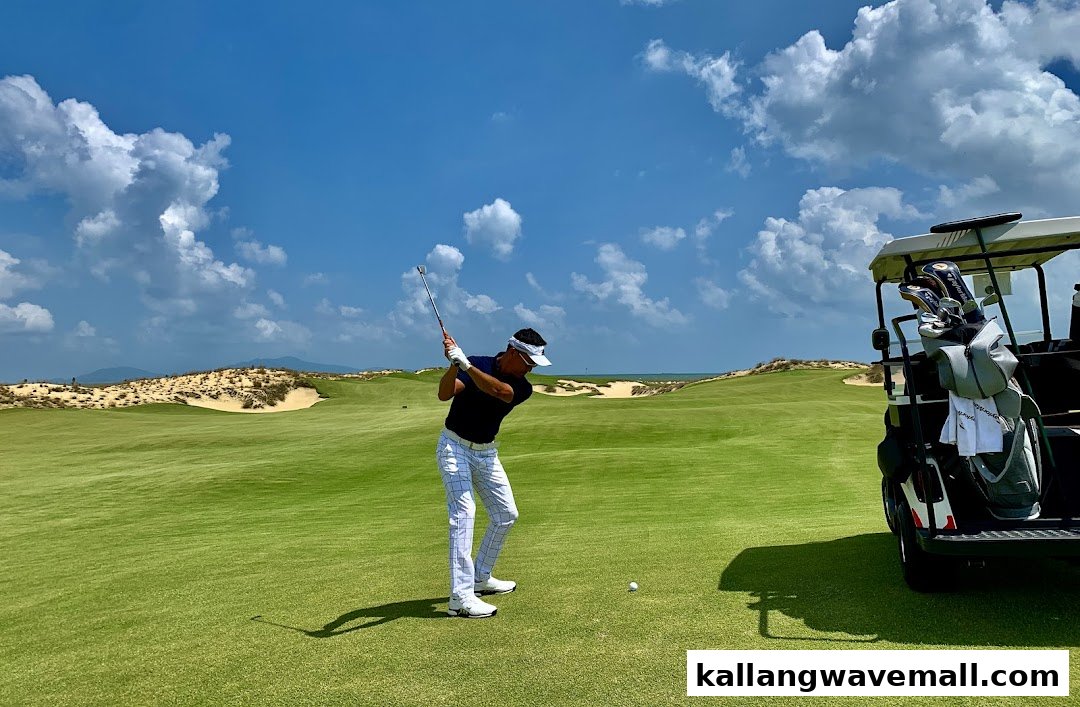 A golfer swings on a lush green course with sand dunes and ocean under a blue sky.