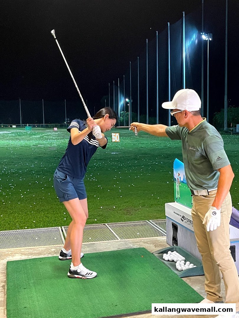 A golf instructor guides a student practicing their swing at a night driving range.
