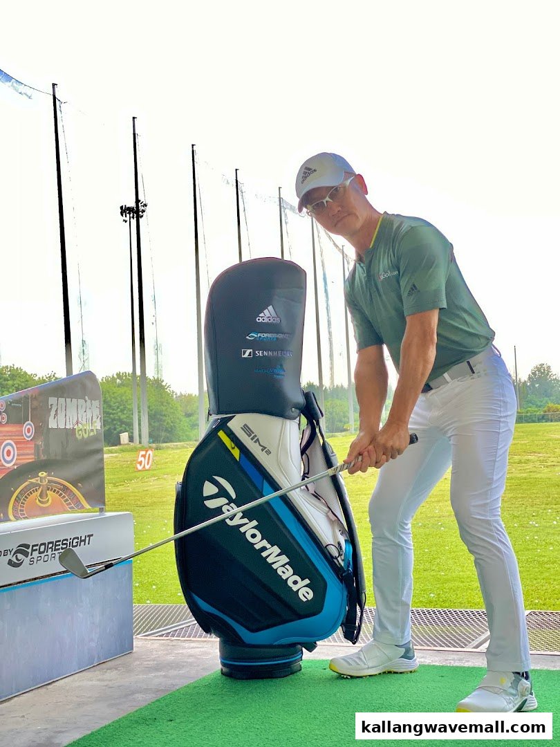 A golfer in Adidas gear practices at a driving range with a TaylorMade bag and Foresight Sports equipment.