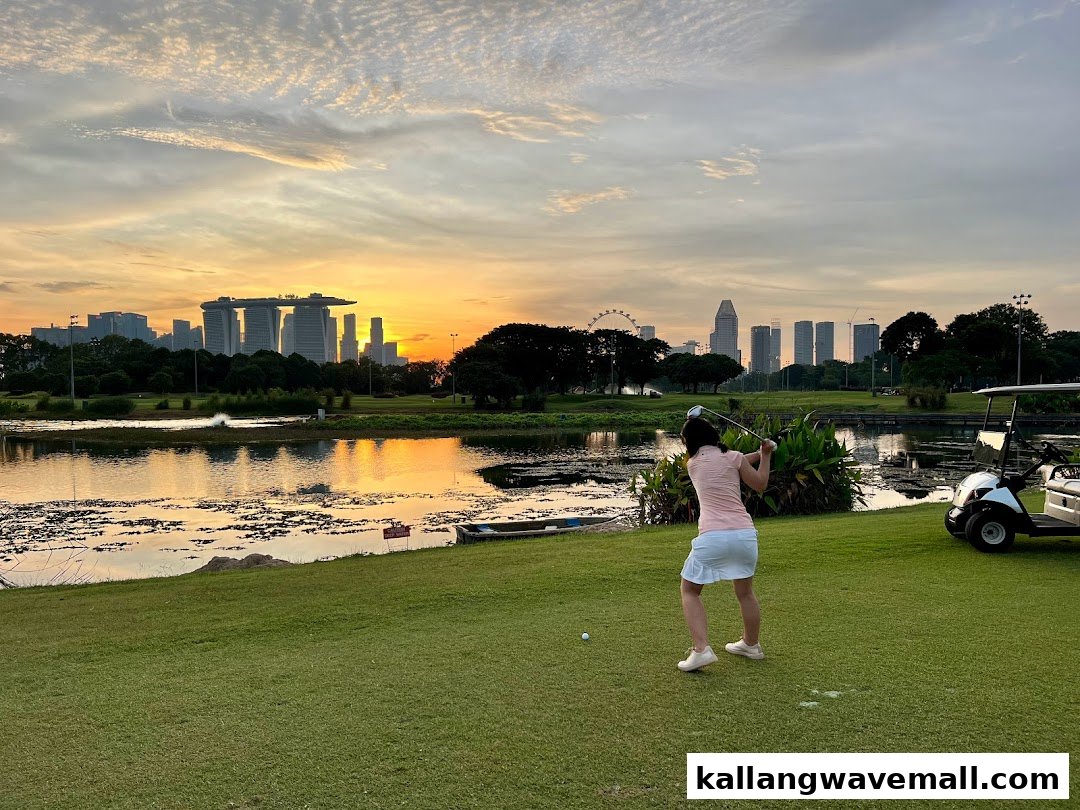 A golfer swings on a scenic course at sunset, with a city skyline in the background.