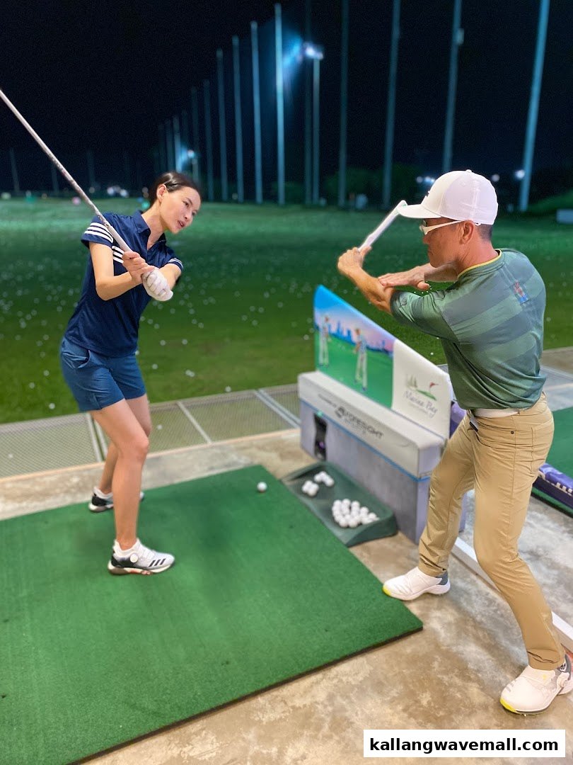 Two people practice golf at a night driving range, with golf balls and equipment visible.