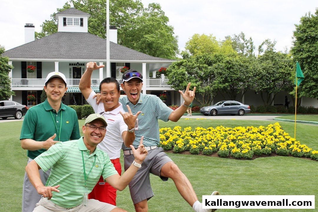Four happy men pose on a golf course with a clubhouse and yellow flowers in the background.