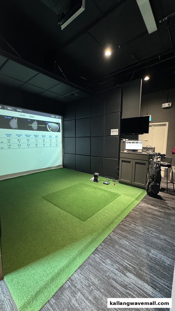 An indoor golf simulator bay with a large projection screen displaying golf data and artificial turf.