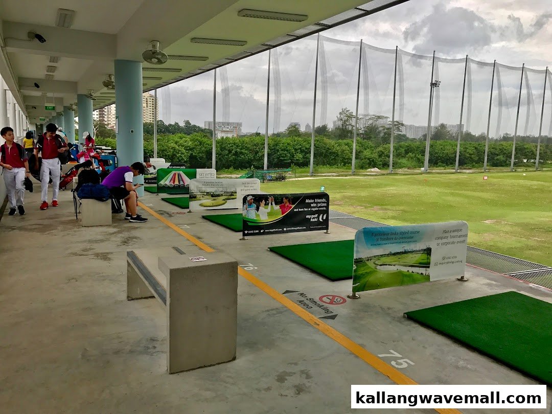 People practice golf at an indoor driving range with multiple hitting bays and a large outdoor net.