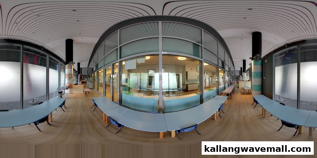 A bright, spacious hallway with tables, leading to classrooms visible through large glass windows.