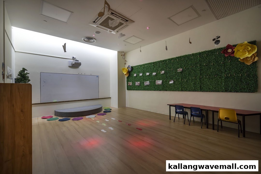 A spacious, brightly lit classroom with a whiteboard, projector, and a green wall decorated with photos.