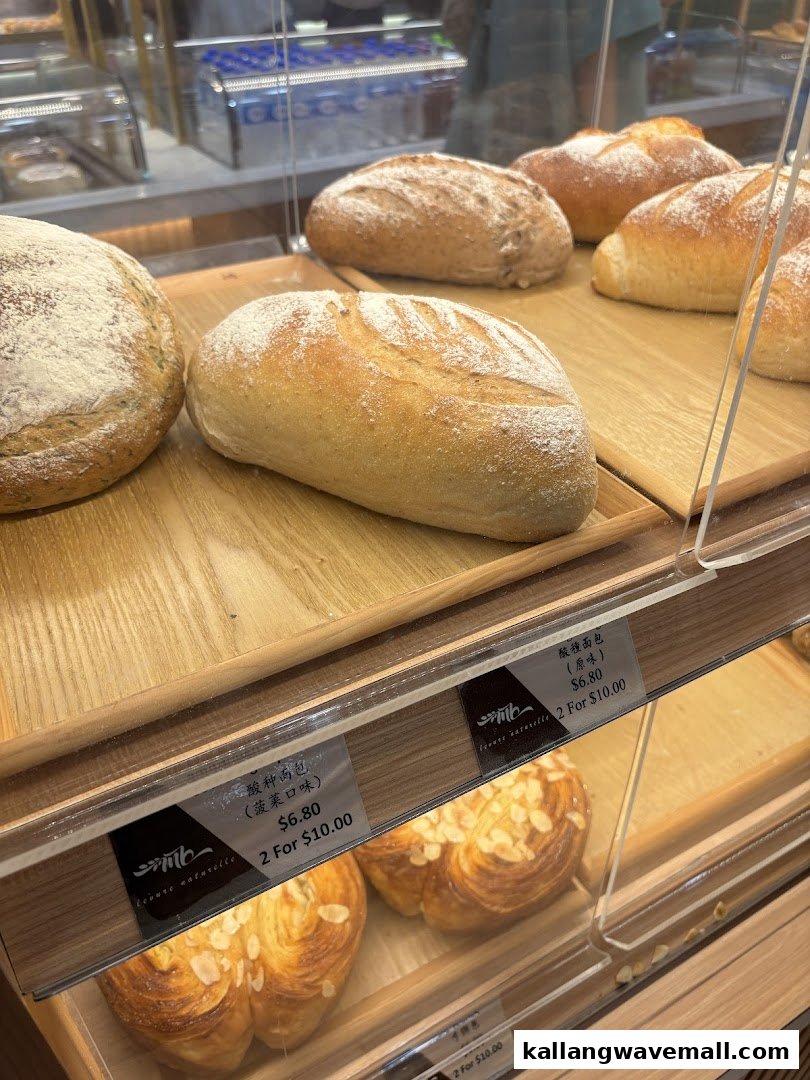 A display case showcasing various freshly baked breads and pastries, including sourdough loaves and almond croissants, with price tags.