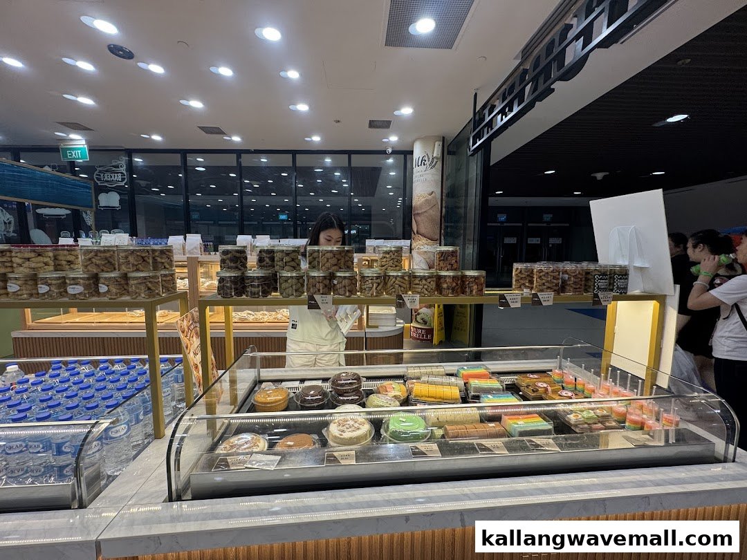 An interior view of MK Levure Naturelle, showcasing a vibrant display of cakes, cookies, and bottled water, with a staff member attending.