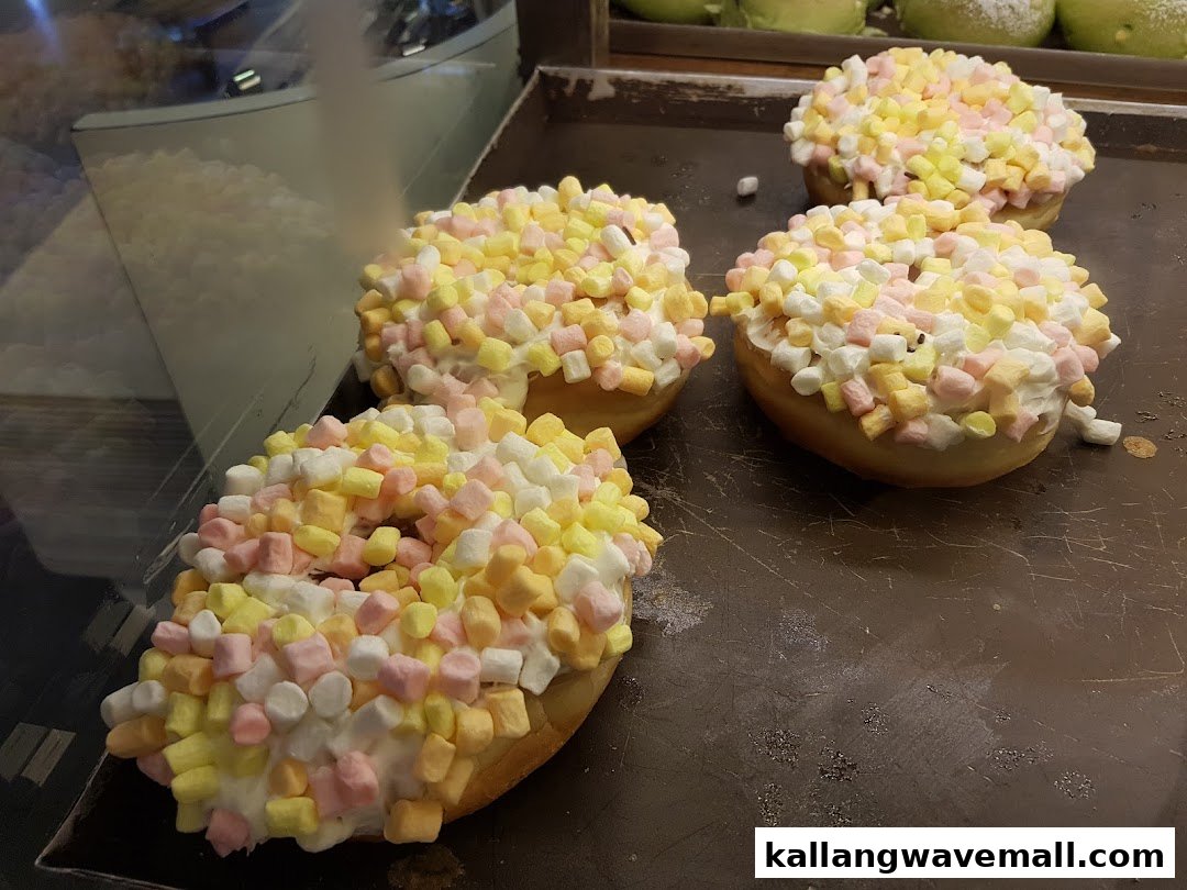 Four marshmallow-topped donuts on a baking tray in a display case.