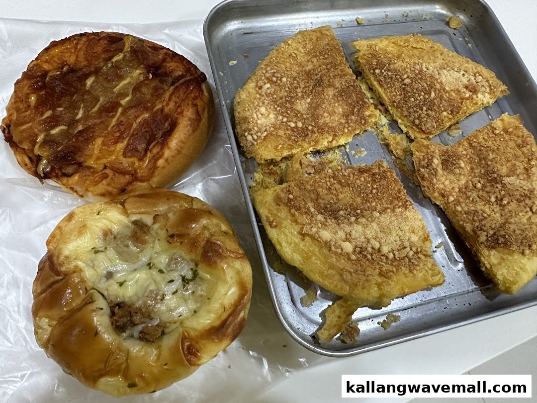 A close-up of freshly baked savory buns and golden, flaky pastries on a metal tray.