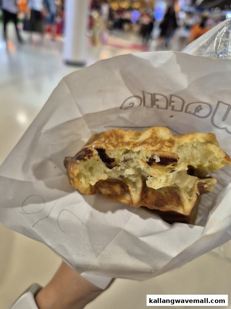 A hand holds a freshly baked waffle with chocolate chips in a paper bag.