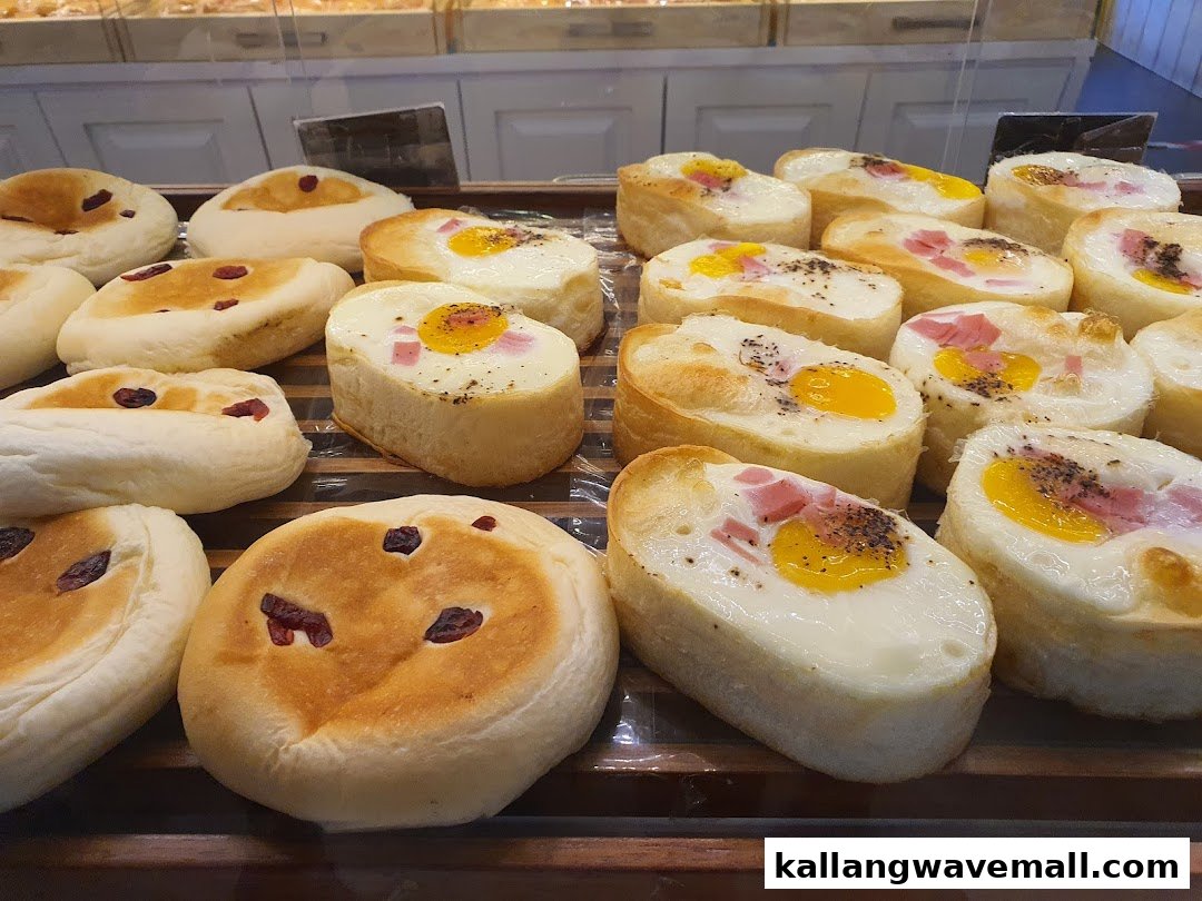 A display of freshly baked bread and pastries, including savory egg and ham buns and sweet fruit buns.
