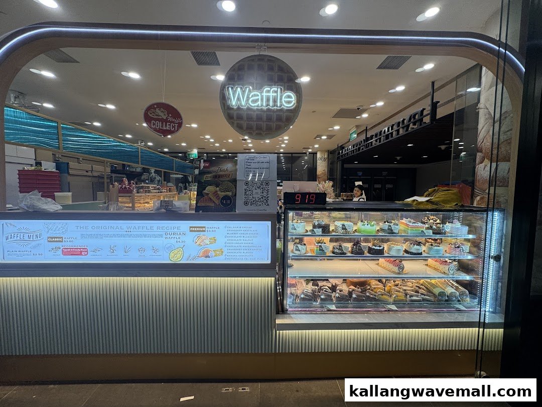 A brightly lit storefront of a waffle and cake shop, featuring a display case of desserts and a menu board.
