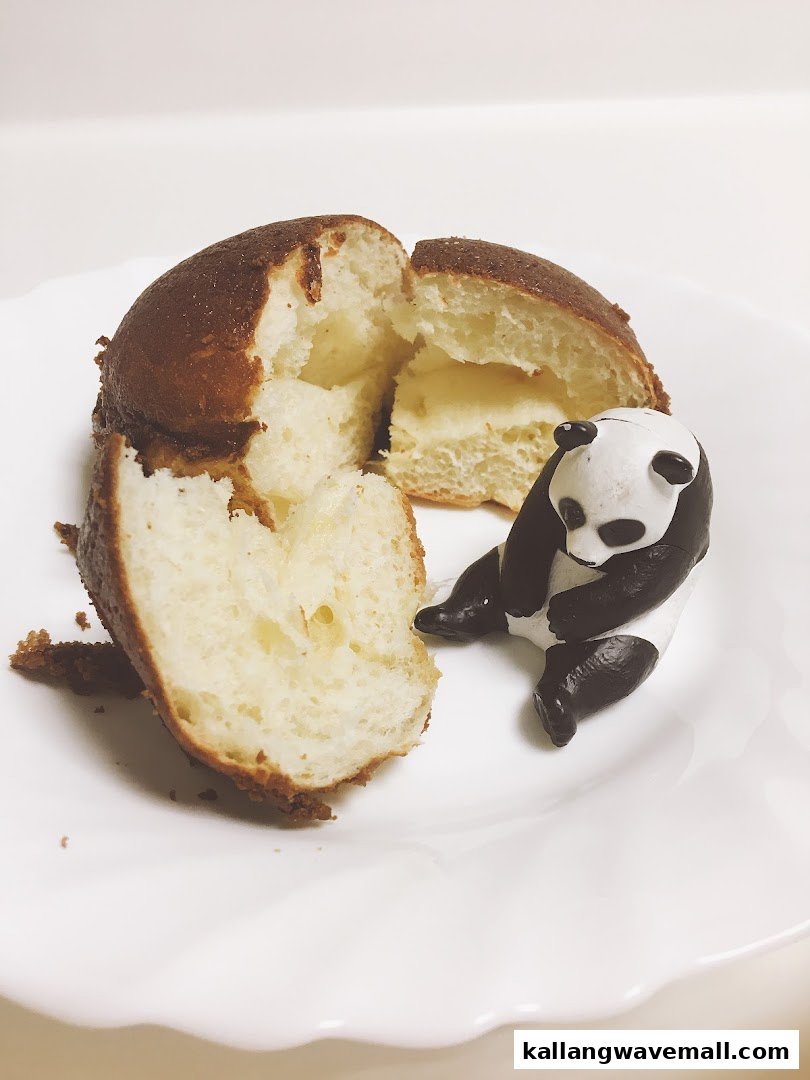 A split sweet bun with a creamy filling on a white plate, next to a small panda figurine.