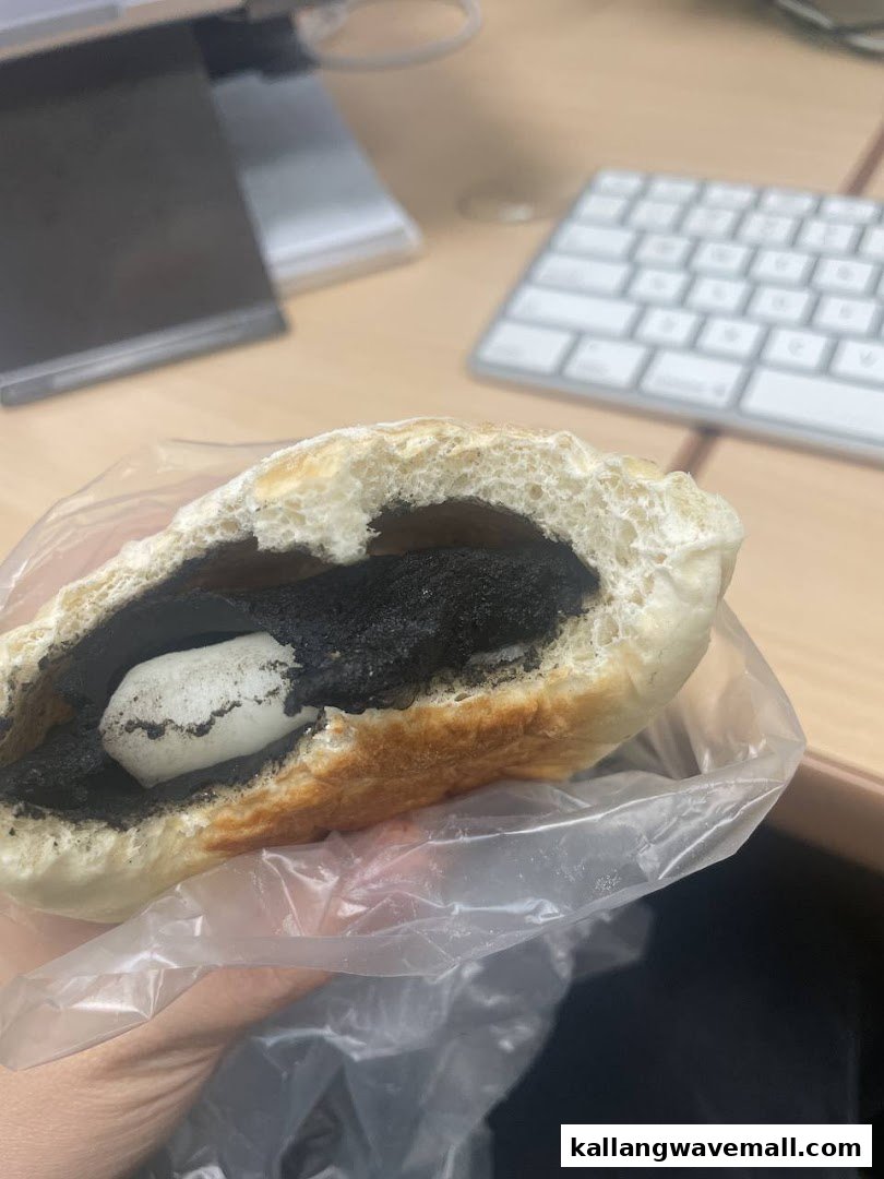 A hand holds a bun filled with black sesame paste and a white mochi-like center, with a desk in the background.