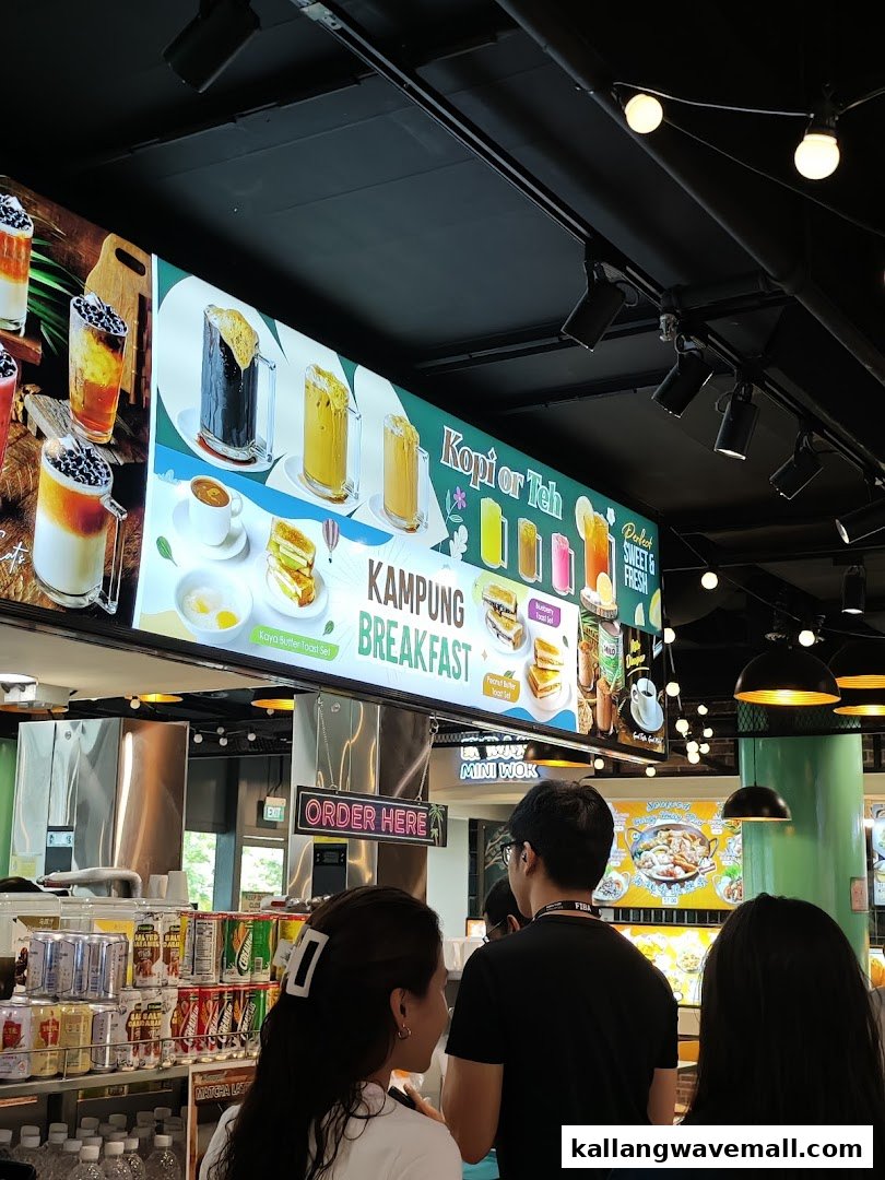Customers queue at a counter under a vibrant digital menu board showcasing traditional breakfast sets and beverages.