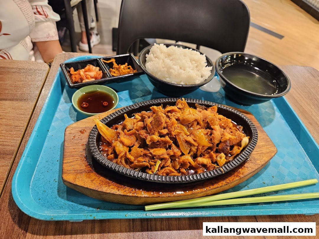 A delicious meal featuring a sizzling meat dish, rice, soup, and side dishes served on a tray.