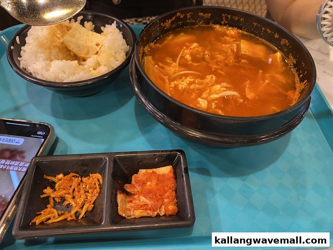 A hearty meal featuring spicy soup, rice, and two side dishes served on a blue tray.