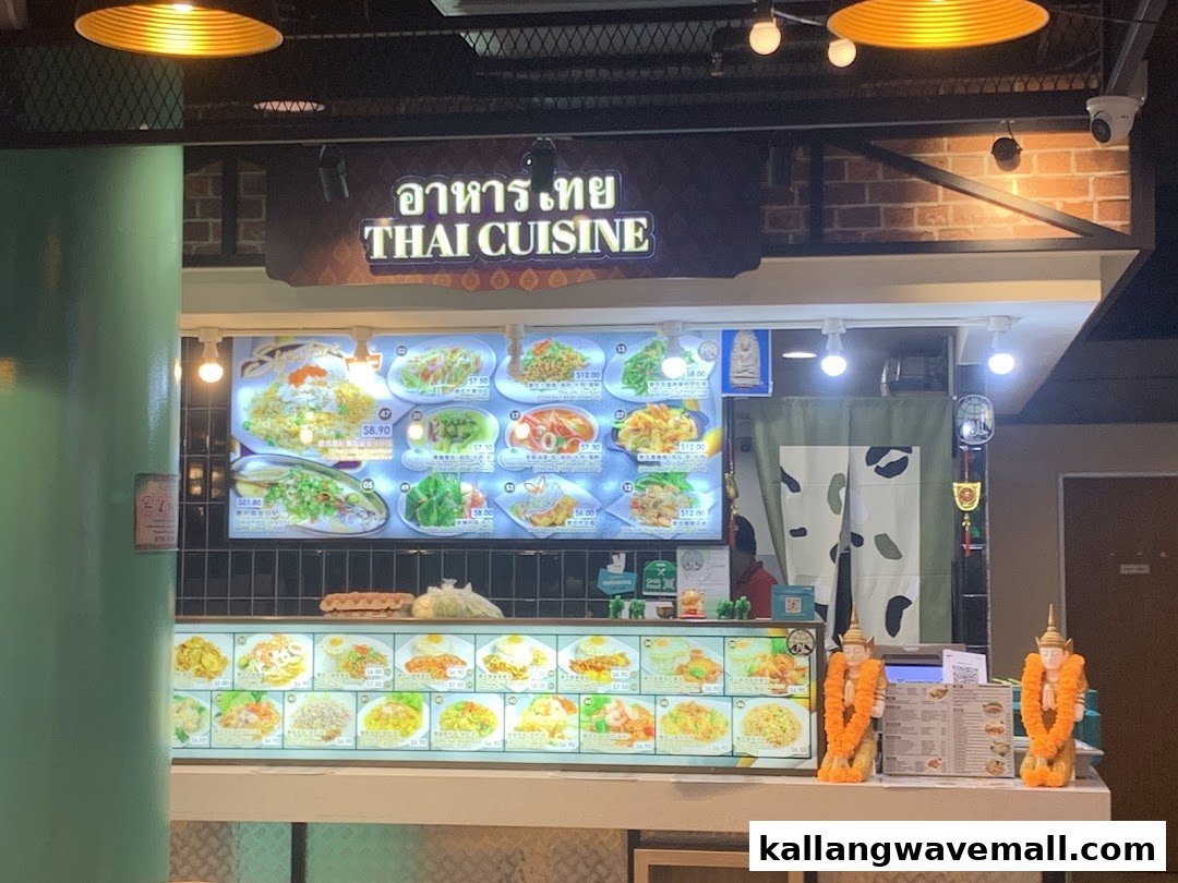 A vibrant Thai food stall displaying a wide array of dishes and prices on illuminated menu boards.