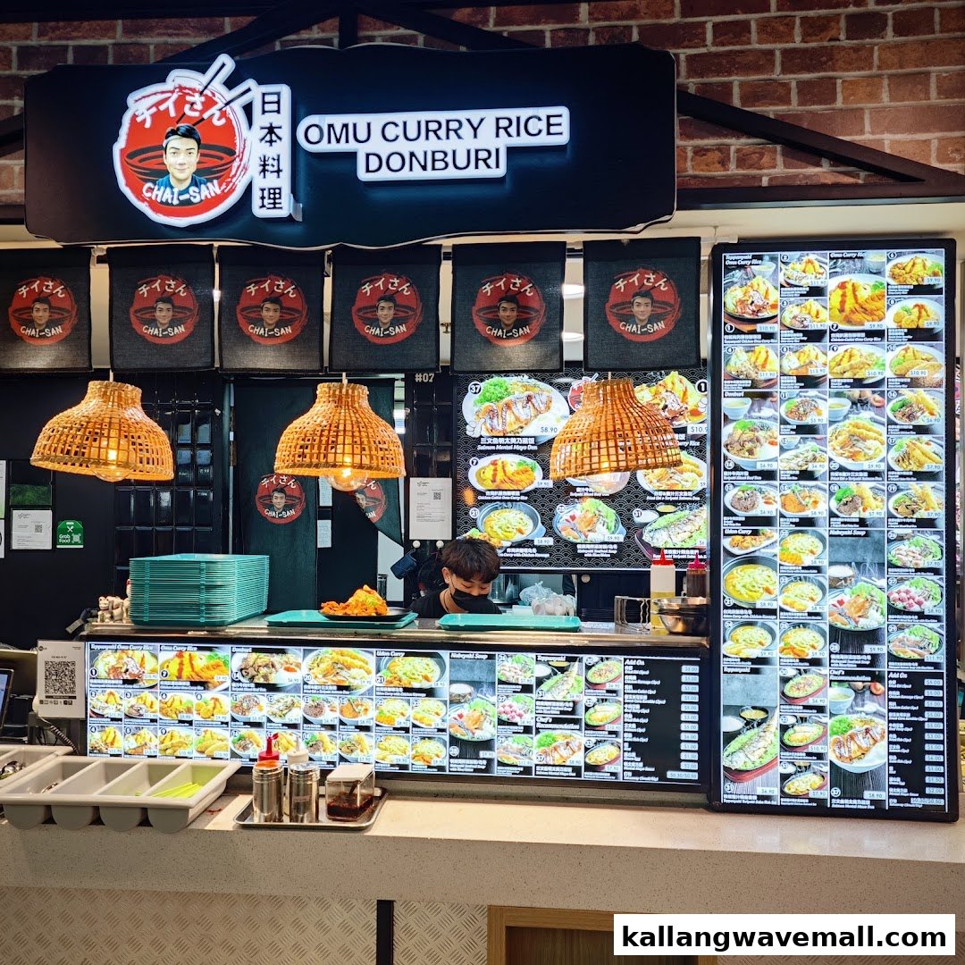 A vibrant food stall counter featuring extensive digital menus for Omu Curry Rice and Donburi, with a staff member preparing food.