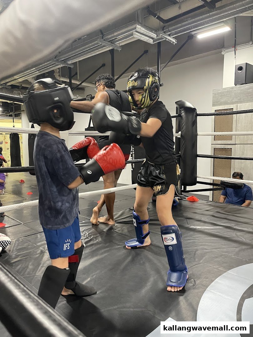 Two individuals in protective gear spar in a boxing ring at Neue Fit, with an instructor observing.
