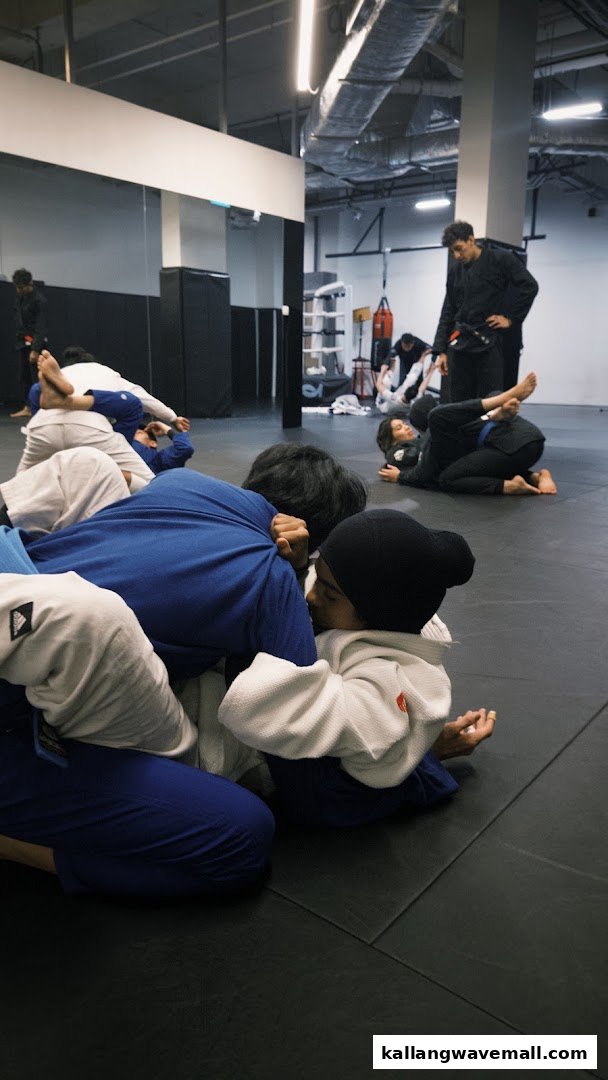 Individuals in gis engaged in martial arts training on a mat, with an instructor observing.