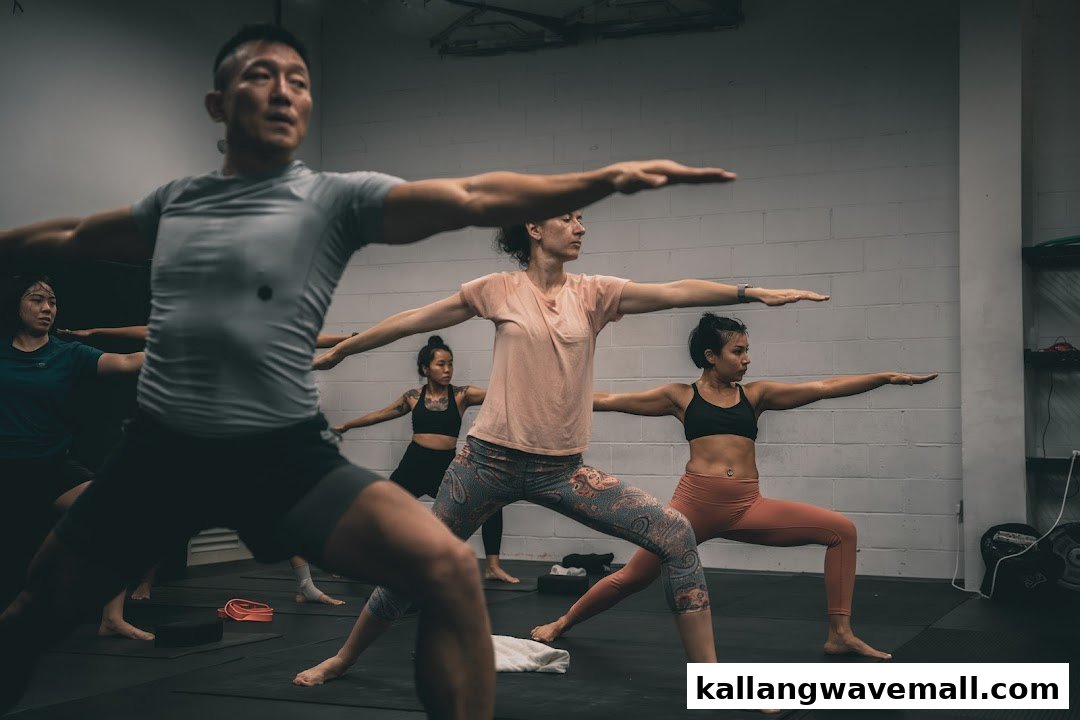 People of various ages participate in a group fitness or yoga class, holding a warrior pose.