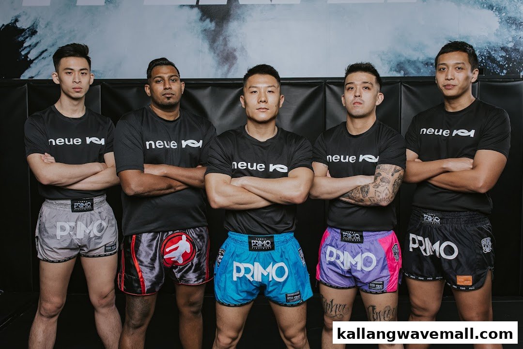 Five men in Neue Fit branded shirts and Primo shorts stand with crossed arms in a gym setting.