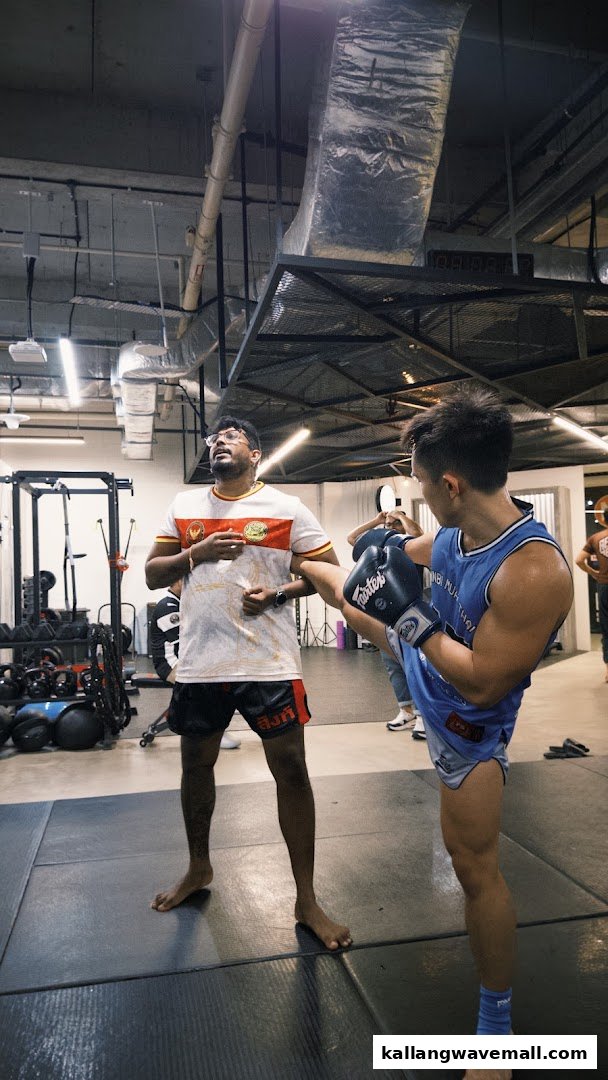 An instructor guides a student practicing a kick in a modern martial arts gym.