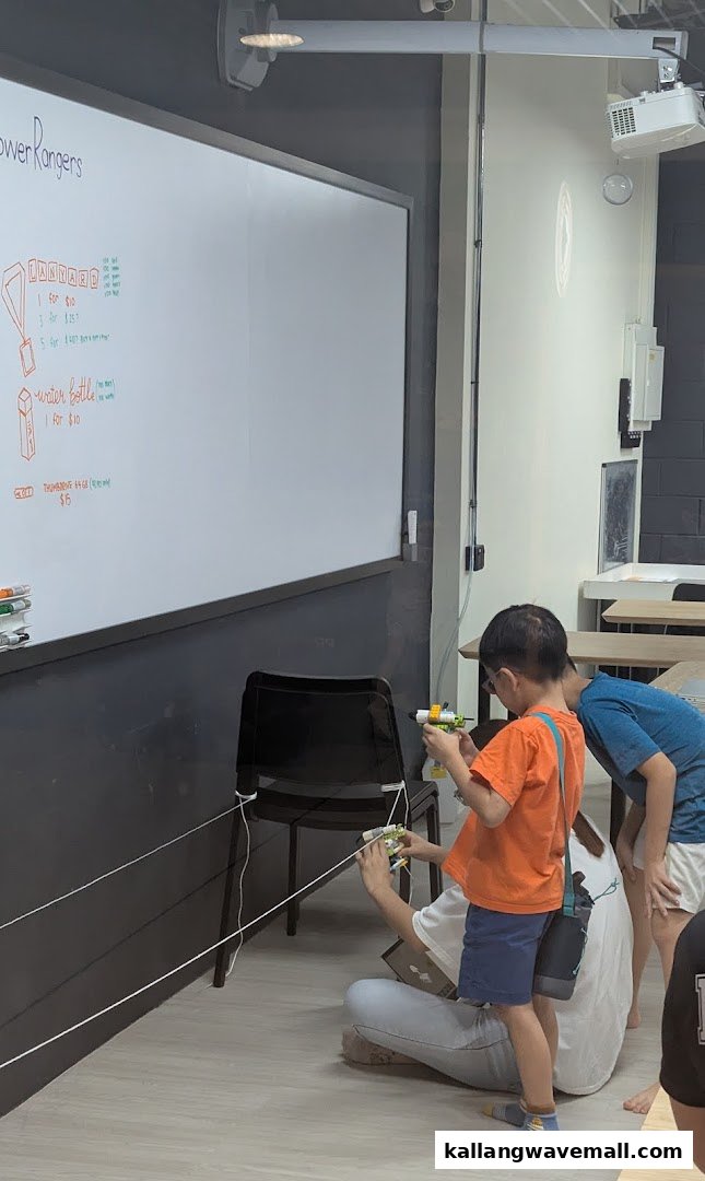 Children and an adult engaged in a robotics activity, with a whiteboard displaying items and prices.
