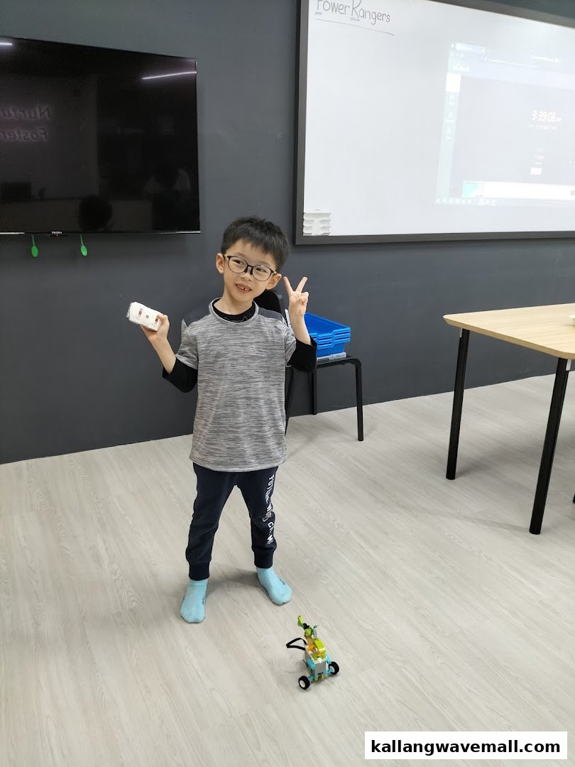 A young boy proudly displays his robot creation in a robotics workshop.