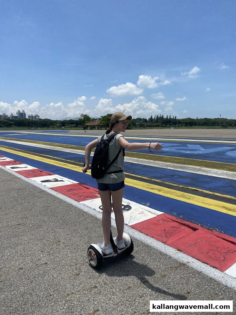 A person rides a mini Segway on an outdoor track under a bright blue sky.