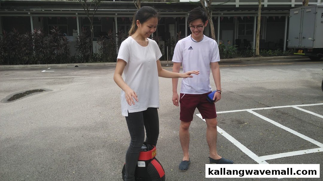 Two people learning to ride a mini segway-like device outdoors.
