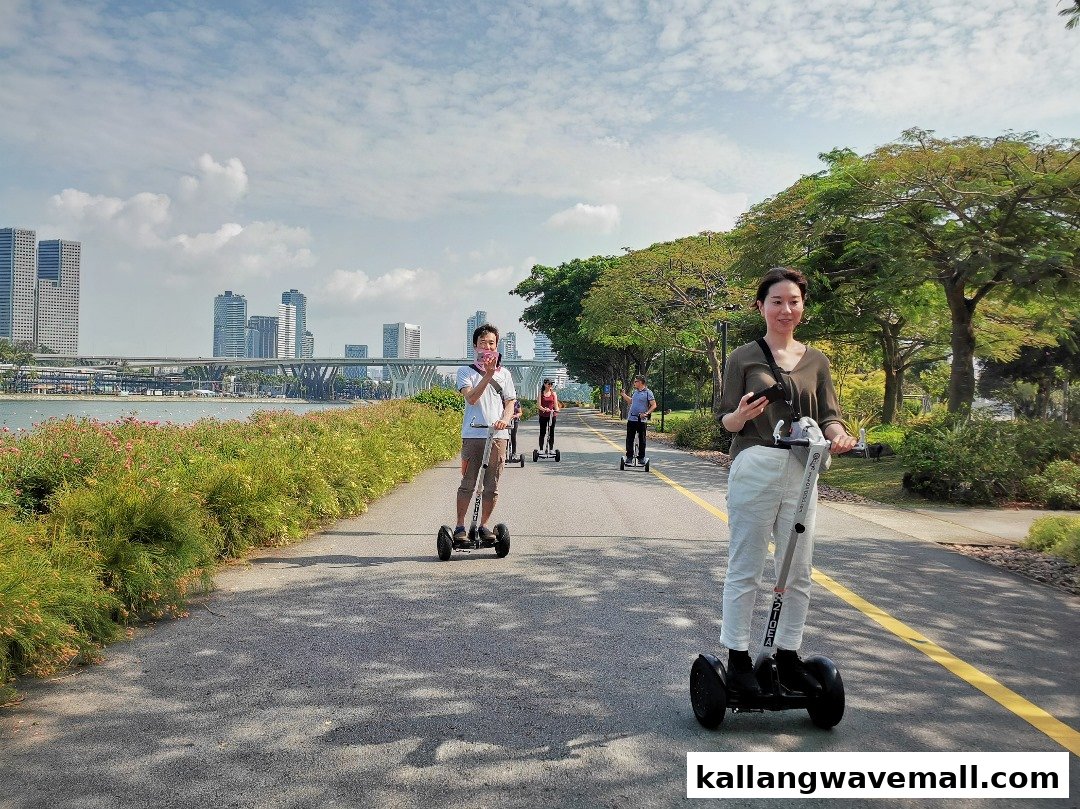 People enjoy riding mini segways on a scenic path with a city skyline in the background.