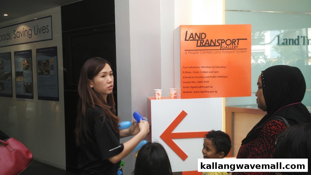 A staff member interacts with visitors near the Land Transport Gallery sign, detailing tour schedules.