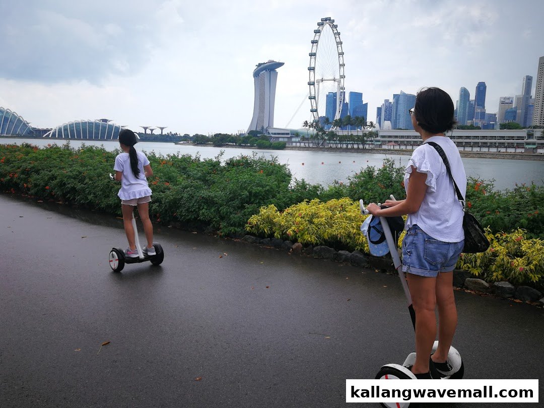Two people ride mini Segways along a scenic waterfront path with Singapore landmarks in the background.