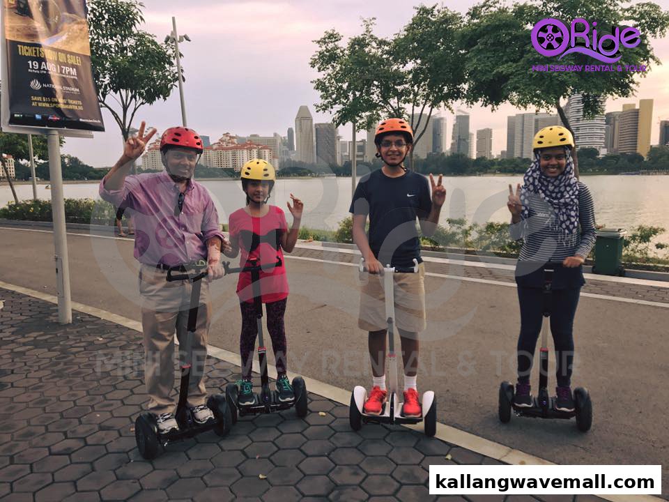 Four people on mini segways, wearing helmets, smiling outdoors with a city skyline in the background.