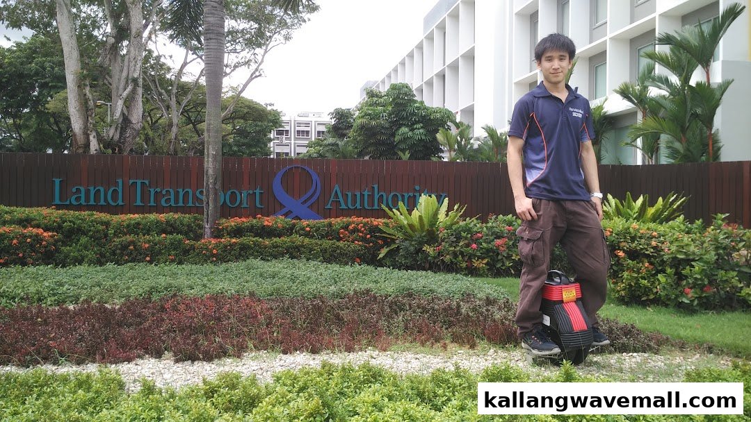 A person stands with a mini segway-like device in a garden setting, near a 'Land Transport Authority' sign.