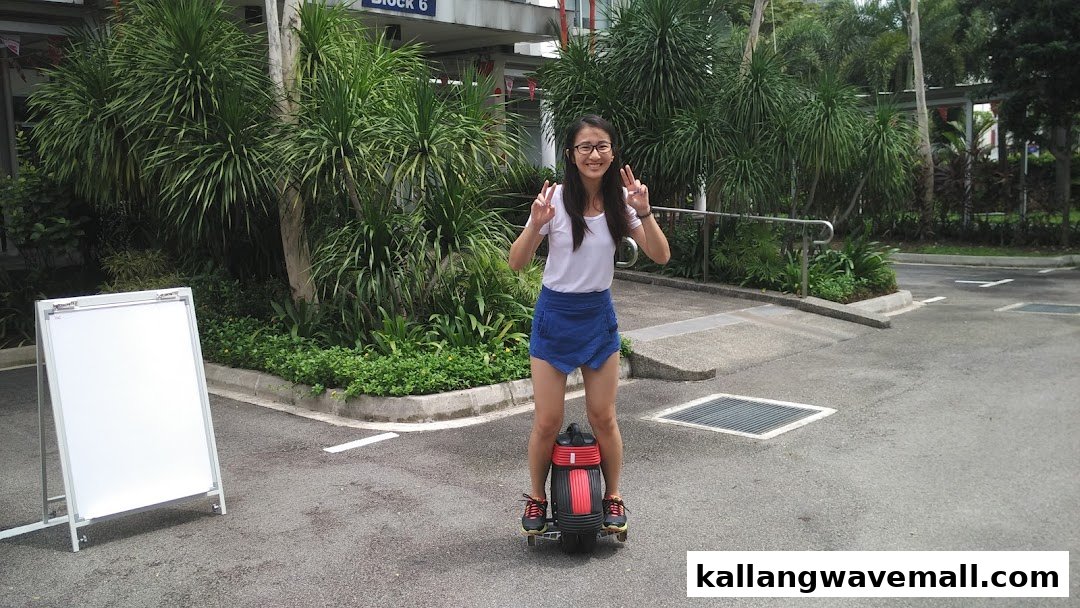 A young woman smiles while riding a mini segway outdoors, making a peace sign.