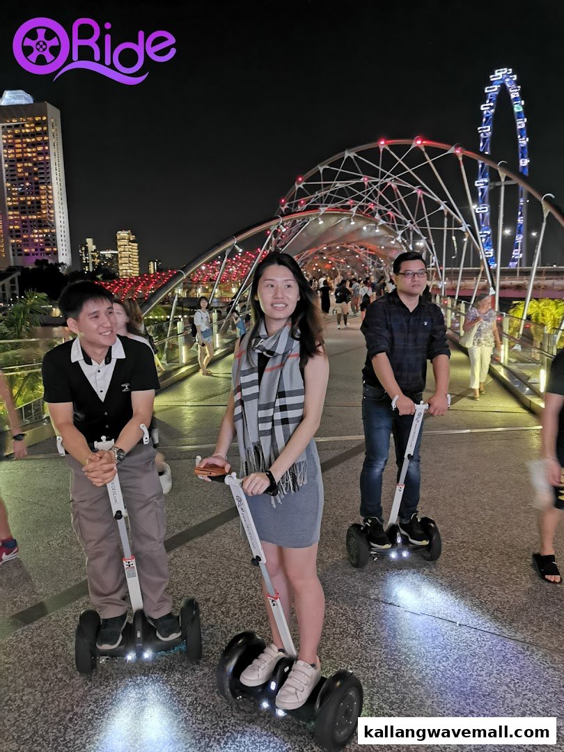 People enjoy riding mini segways on a scenic bridge at night, with city lights in the background.