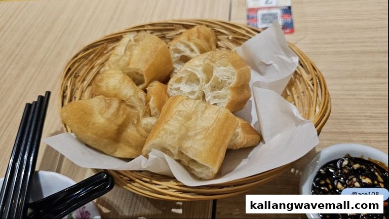 A basket of golden-brown fried dough sticks (youtiao) with a side of dark dipping sauce.