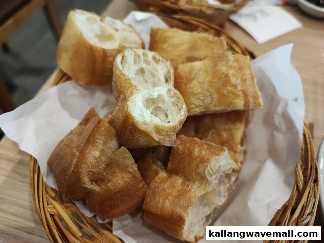A close-up of golden-brown fried dough sticks (You Tiao) served in a woven basket.