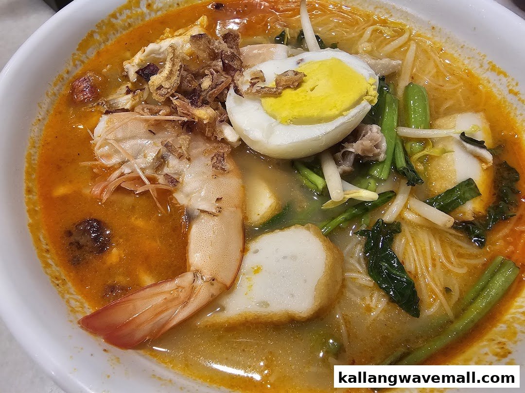 A close-up of a vibrant bowl of curry laksa or prawn noodles with shrimp, egg, and vegetables.