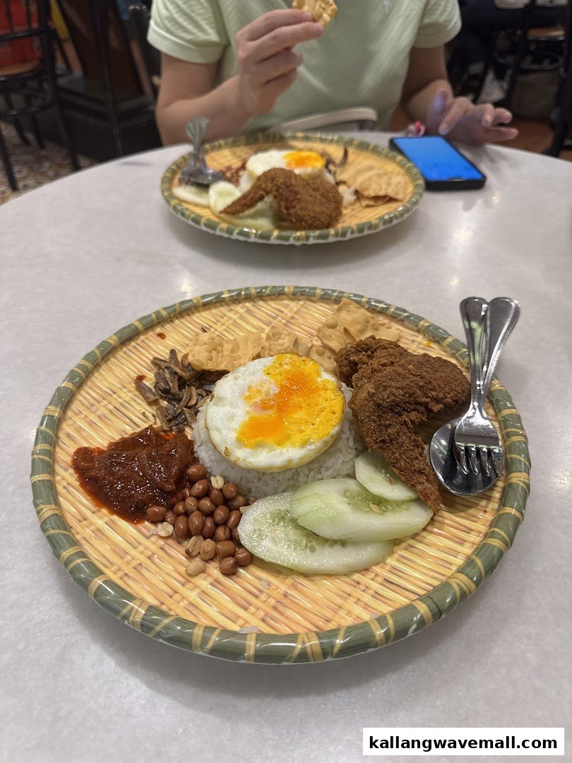 Two plates of Nasi Lemak with fried chicken, egg, and condiments on a table.