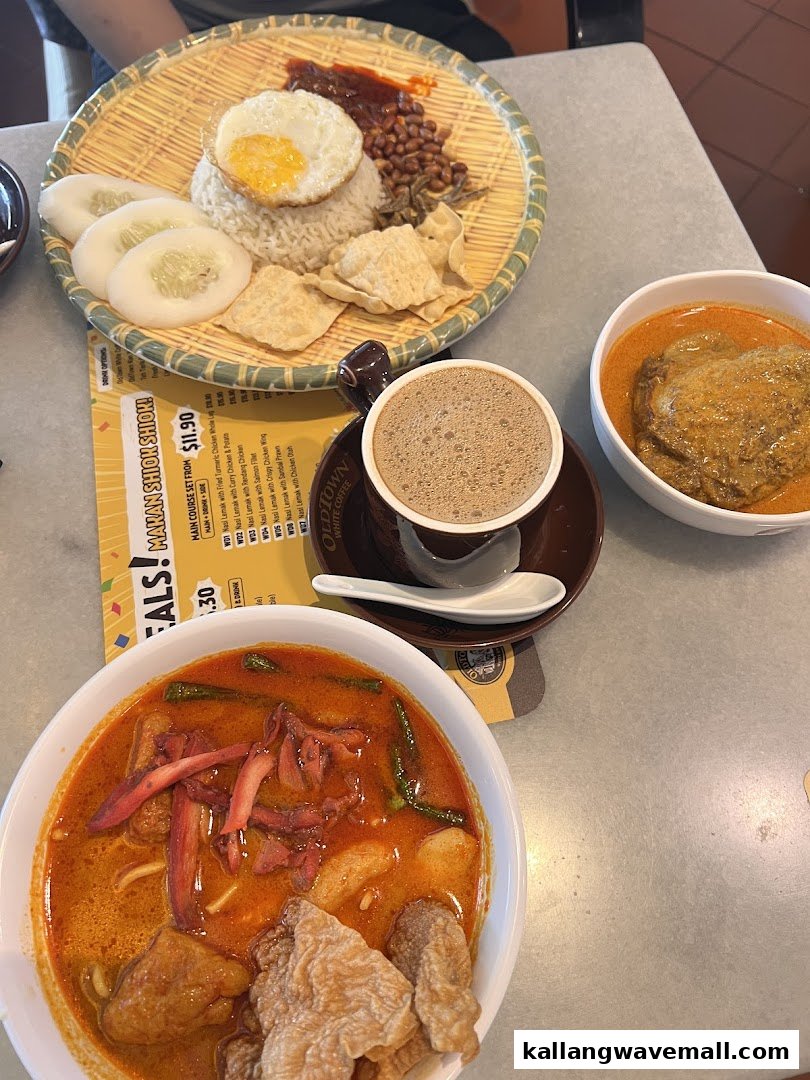 A table laden with Malaysian dishes including Nasi Lemak, curry, and Oldtown White Coffee, with a partial menu visible.
