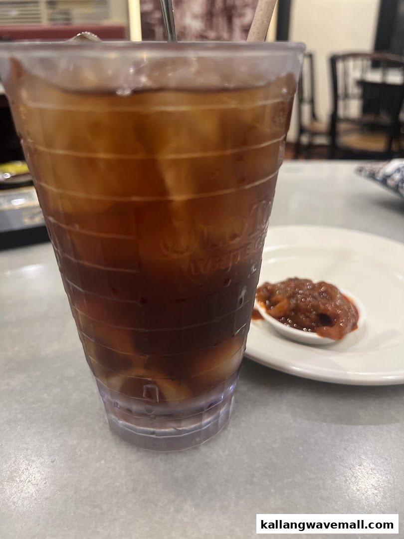 A refreshing iced tea and a small dish of sambal or relish on a table at Oldtown White Coffee.