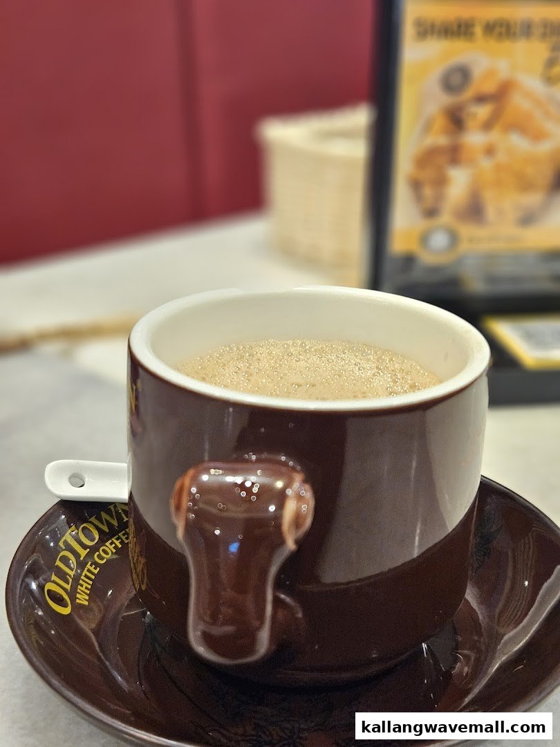 A close-up of a frothy coffee in a branded Oldtown White Coffee cup.