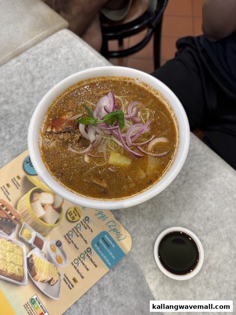 A bowl of Oldtown White Coffee's signature curry noodles with a side of sauce and a partial menu on a table.