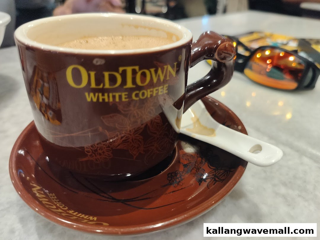 A cup of OldTown White Coffee on a saucer with a spoon, on a table.